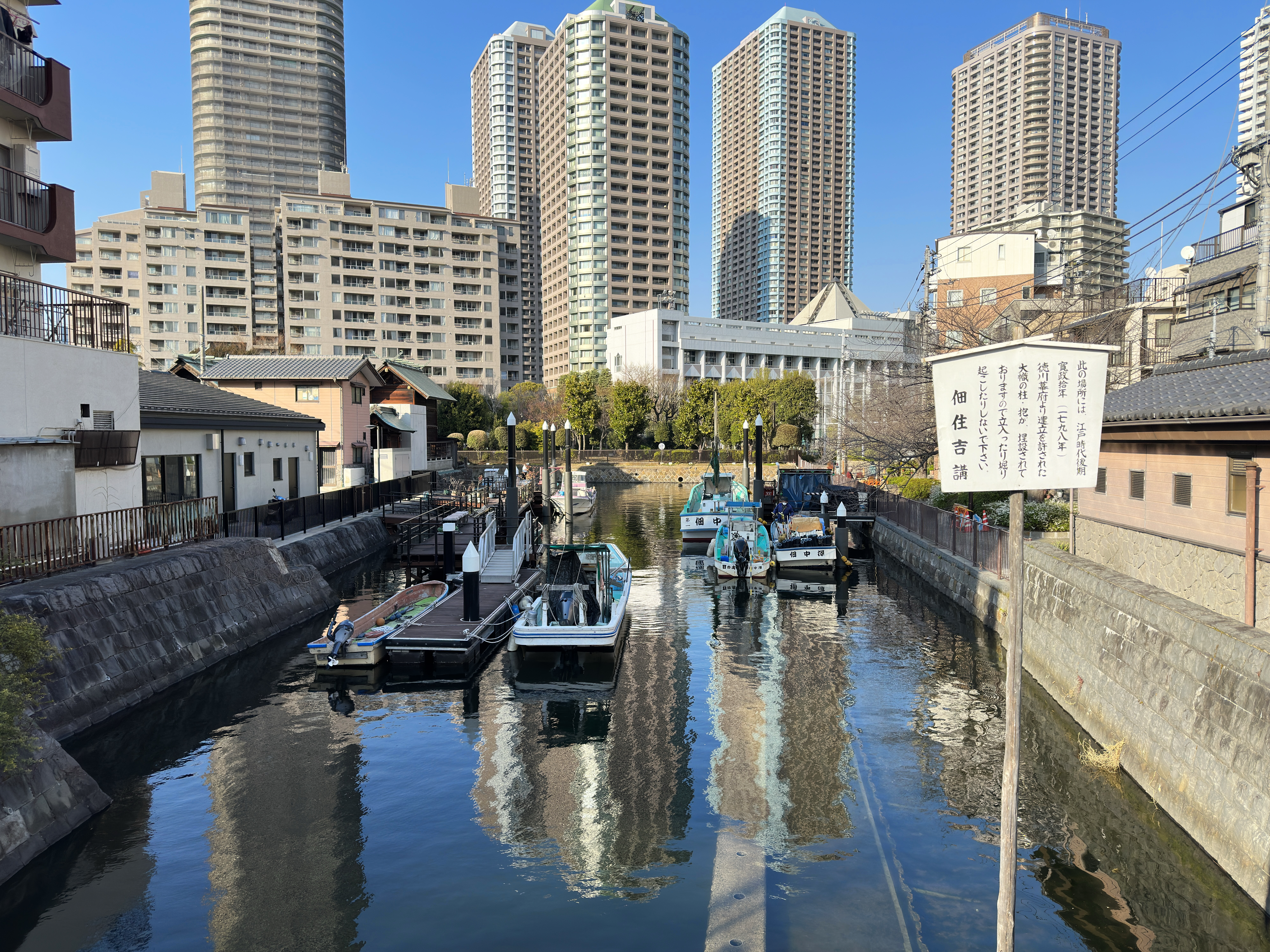 Tower buildings with the moat and the sign indicating the location where the wooden segments are buried on Tsukudajima. © 2026 Kiuchi Kumiko. All rights reserved.